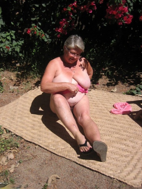 In her tan, the elderly lady known as the Grim Grim Grime Goddess takes off all her clothes and sews herself in her sandals on the garden patio.