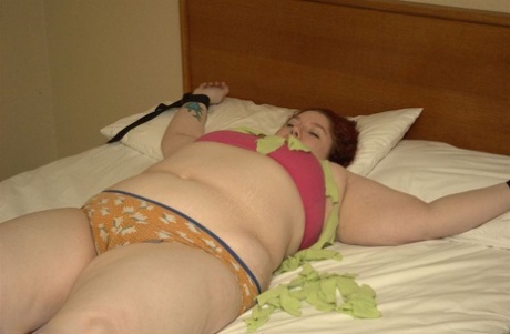 BBW Inkedoracle, an amateur hacker who wears glasses and black jeans, is strapped down to her bed while her clothing falls away.