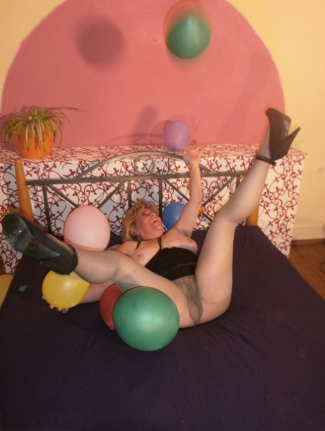 Amid balloons on her bed, Caro exposes her breasts while wearing pantyhose.