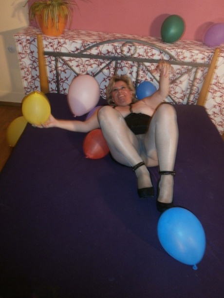 On her bed, an old woman named Caro displays balloons and exposes her breasts with pantyhose.