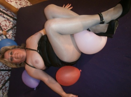 Caro, an elderly woman, exposes her breast tissue in pantyhose while hanging out with balloons on her bed.