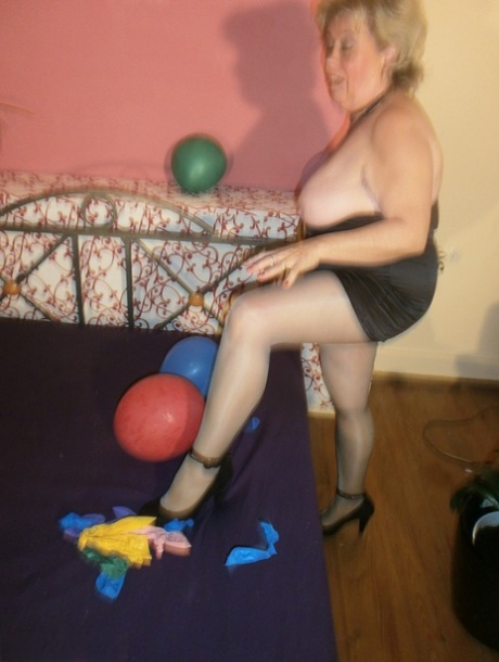 With balloons on her bed and pantyhose covering her thighs, Caro, an elderly woman, exposes the latter to airborne objects.