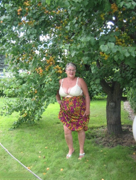 The fat granny girdle goddess exposes her large tits beneath a fruit tree.