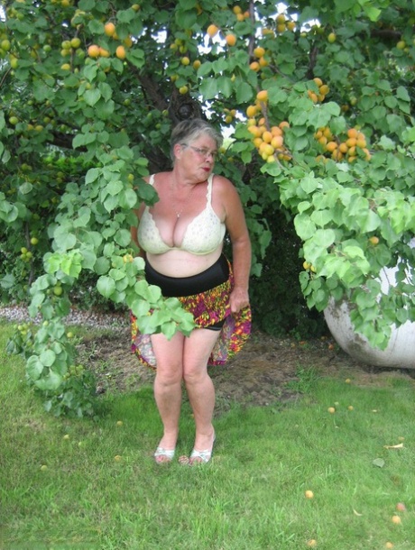 An apple-bearing fruit tree is used by the fat granny Girdle Goddess to conceal her large tits beneath.