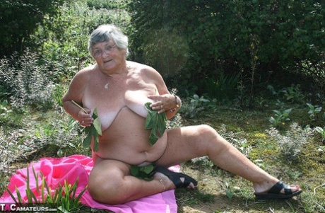 After being exposed on scrubby ground, Grandma Libby, a fat British woman, exposes herself to the elements while naked on a towel.