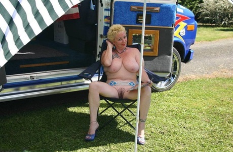 Mary Bitch, who is now mature and blonde, displays her large tits and pussy outside a B class camper van.