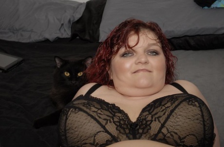 In a bed, Redheaded Black Widow BBW Black Widow AK wears a black bra and pants.