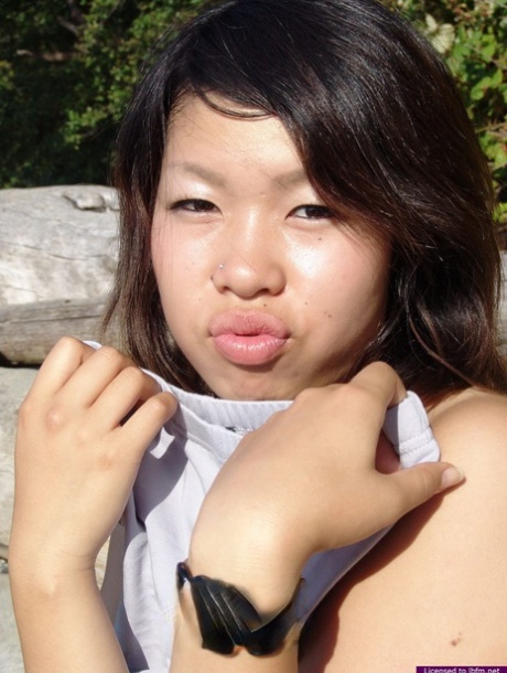 A naked Asian amateur takes a break from smoking on the beach while sitting in driftwood.