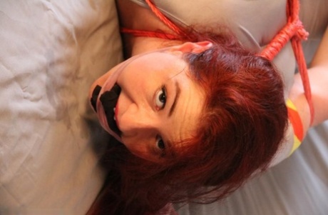 The natural redhead is left on a bed, tied up and gagged.