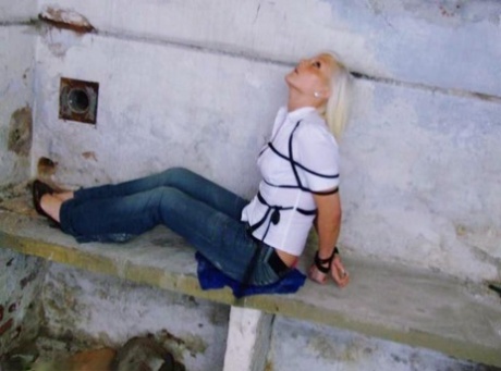 In a pair of blue jeans and white shirt, a British woman is tied up and gagged.