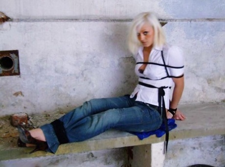 A white shirt and blue jeans are worn by a British woman who is tied up and gagged.