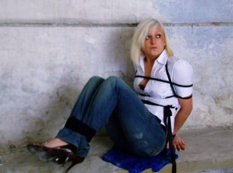 Blue jeans and a white shirt are worn by a British woman who is tied up and gagged.