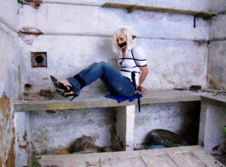 A white shirt and blue jeans are worn by a British woman who is tied up and gagged.