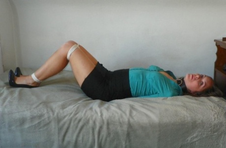 Women are strapped down in a black miniskirt and pumps, tied up on a bed.