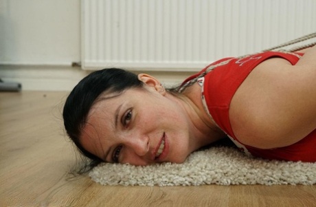 A dark-haired woman is shirking in her clothes on a carpet.