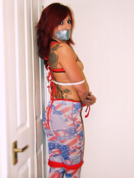 The tattooed redhead is silenced with gags while being held back by ropes.