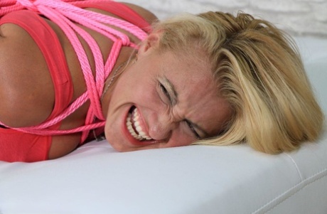 A fully clothed blonde woman grimaces while wearing a pair of black stockings and pink rope.