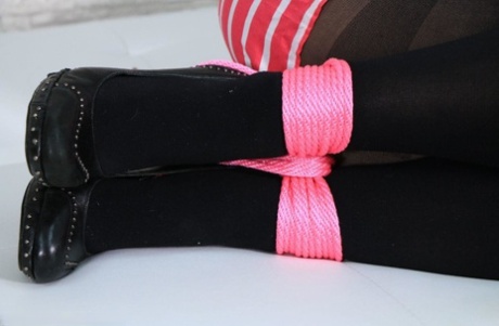 Fully clothed blondes grimace while being tied down with pink rope and wearing black stockings.
