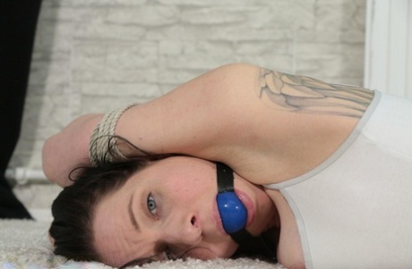 A tattooed woman exposes her augmented tits while being restrained and ball gagged.