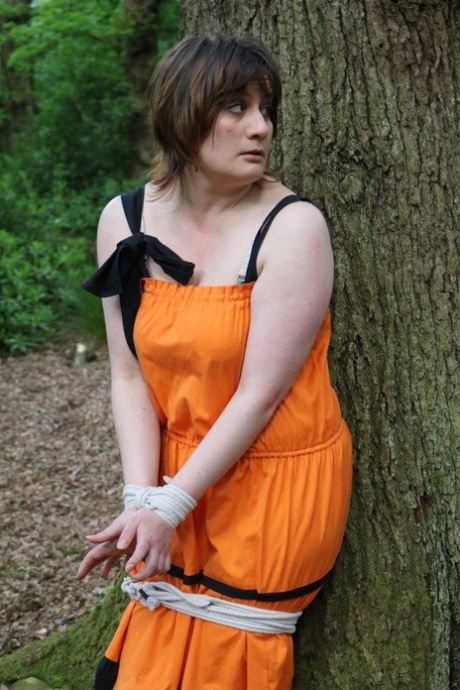 In the woods, a fat woman is tied down by a tree and put on her clothes.