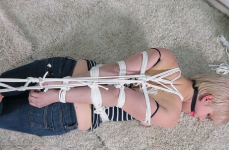 Despite the ball gag and rope bindings, an attractive white girl struggles with her feet.