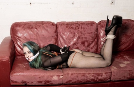 A white girl with dyed hair finds herself on a Chesterfield, gagged and tied up.