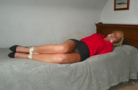 Blonde woman tied up on a bed while wearing cleaved in her clothes.