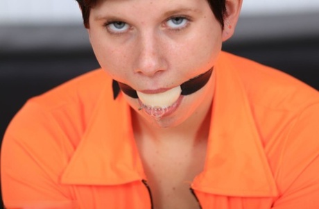 A girl with ball-gagging and short hair is wearing cuffs at her wrists, ankles, elbows, and both ends.