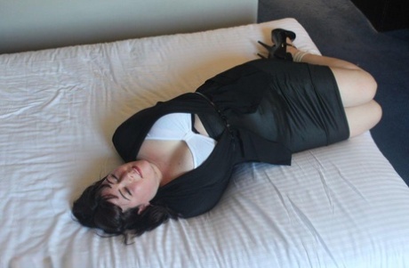 The brunette lady displays her breasts on a bed, bound and gagged.