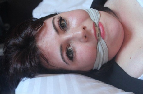 The dark-haired lady exhibits her breasts on a bed, bound and gagged.