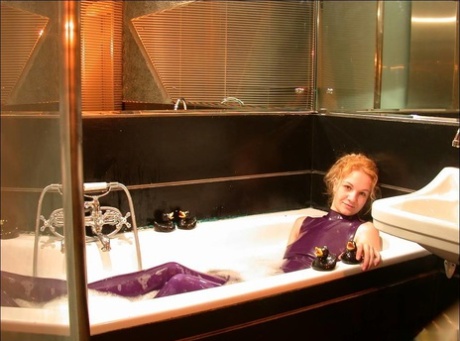 The naked feet of a white girl are observed while she takes a bath in purple latex clothing.