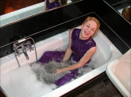 While in the bath, a white girl wears purple latex clothing and displays her bare feet.