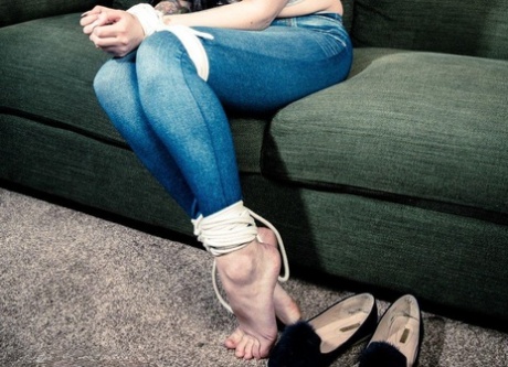 Wearing an arm around the ankles and bound in a big ball gag, this dark-haired girl is seen with her hands on the legs.