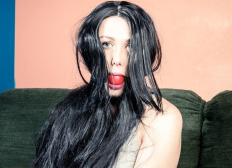 A dark-haired girl performs a big ball gag while being restrained at her wrists and ankles.