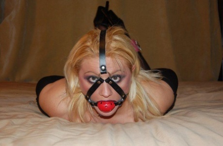 Blonde chick in crotchless bodystocking is restrained and ball gagged on a bed