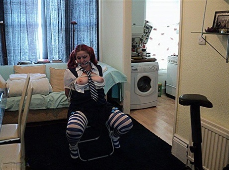 This is a schoolgirl with heavy hair and red hair who is tied up to a chair while wearing tights in her cleave.