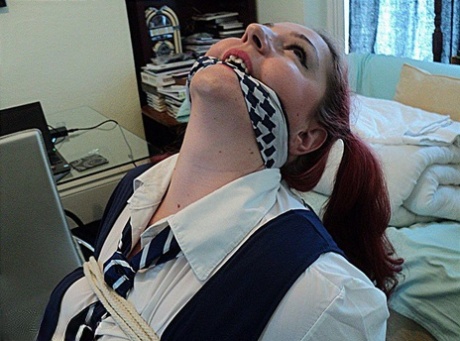 Despite being overweight and having red hair, the schoolgirl is still tied up to an armoire while being gagged with her legs in place.