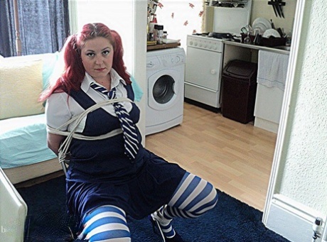 While being restrained by a chair, an overweight schoolgirl with red hair is shown wearing tight clothes and having her cleaved off.