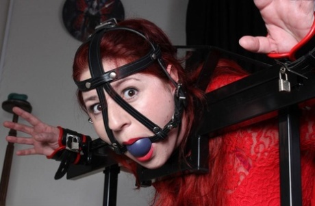 Redheaded Chick Receives A Flogging While Ball Gagged In Stocks