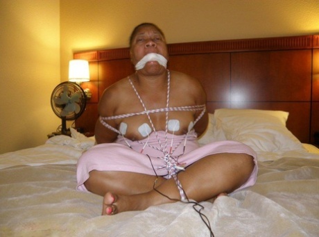 Ebony fatty gets electrical shocks on the bed where it's tied up and gagging on a bedside.