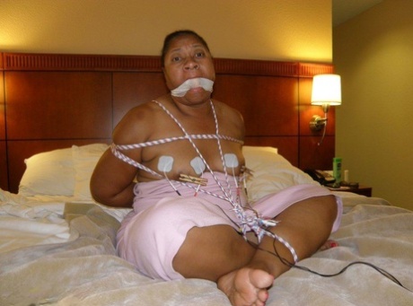 On a bed tied up and gagged, an Ebony fatty gets electrically shocked.