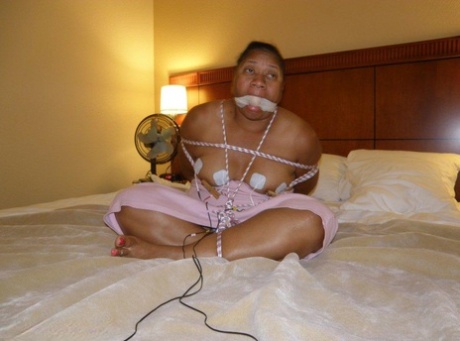 An ebony fat is electrically shocked while lying on a bed, tied up and gagged.