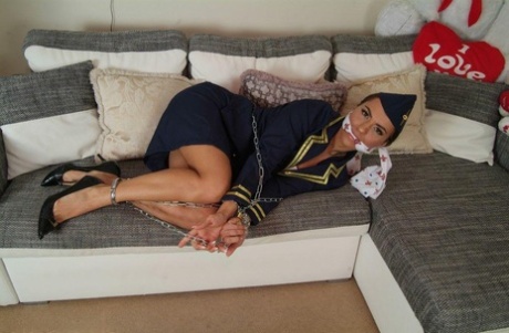 While restrained and gagged, a hot female stewardess is left in her uniform on a sofa.