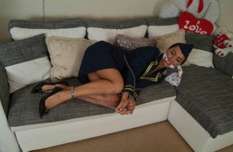 While restrained and gagged, a hot female stewardess is left in her uniform on a sofa.