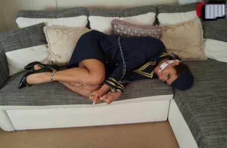 A hot stewardess is left in hiding on a sofa, wearing only her uniform and being restrained and gagged.