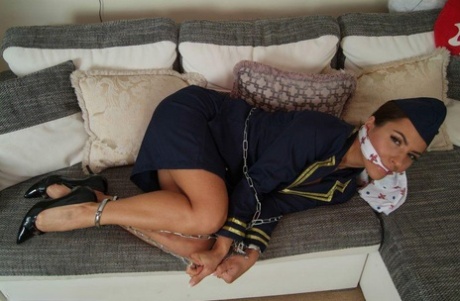 In her uniform, the hot stewardess is left in a snug position on a sofa, restrained and gagged.