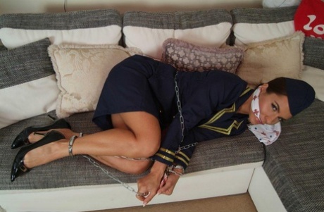 Restricted and gagged: A hot stewardess sits on a sofa in her uniform while being restrained and gagged.