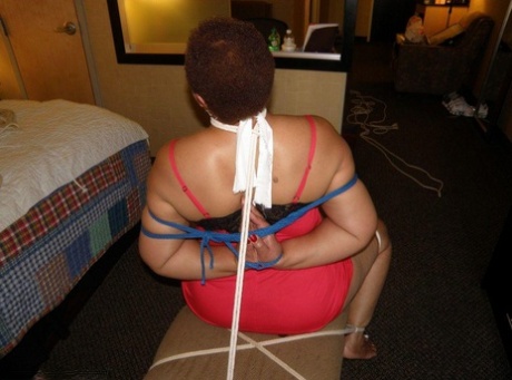 While tied down on a coffee table, an ebony plumper is seen wearing the same booty with its legs in place.