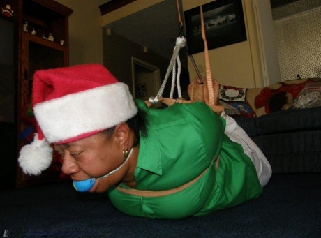 Ball gagged, a fat black woman is tied up in a Santa hat.