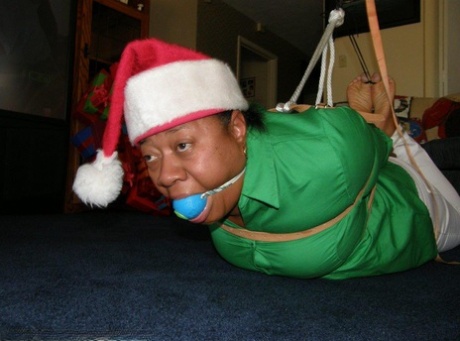 A black woman who is overweight is tied down in a Santa costume and given the ball gagged.